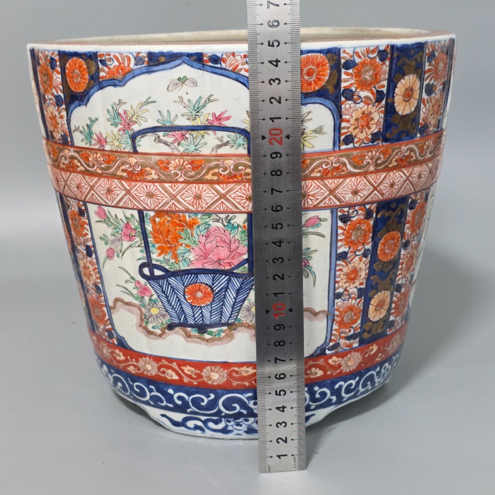 A late 19th-century Japanese Imari porcelain planter decorated with cobalt blue and iron-red floral basket panels, resting on a carved dark wood stand. View V
