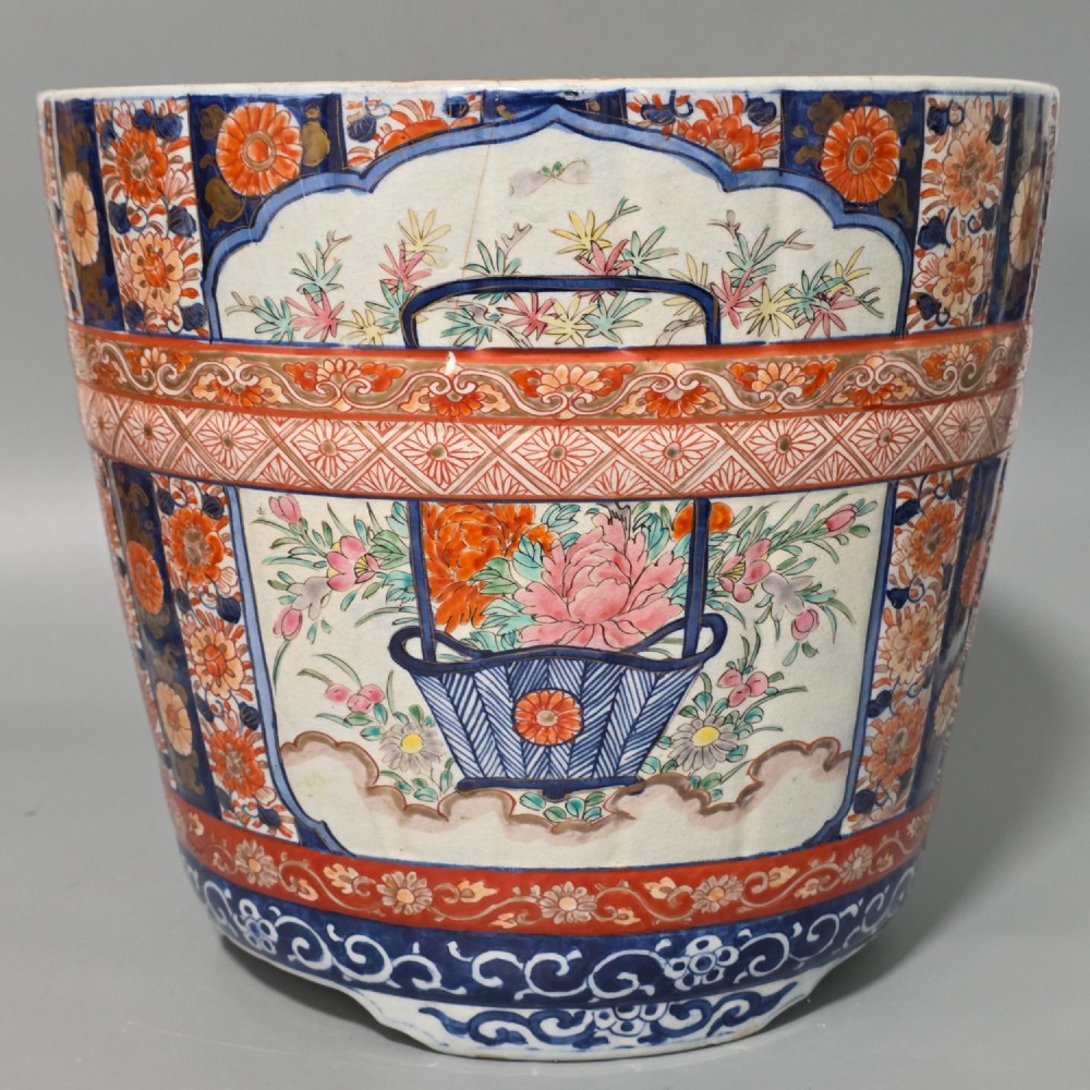 A late 19th-century Japanese Imari porcelain planter decorated with cobalt blue and iron-red floral basket panels, resting on a carved dark wood stand. View VI