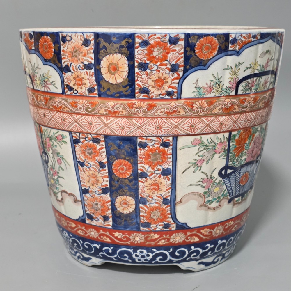 A late 19th-century Japanese Imari porcelain planter decorated with cobalt blue and iron-red floral basket panels, resting on a carved dark wood stand. View VII