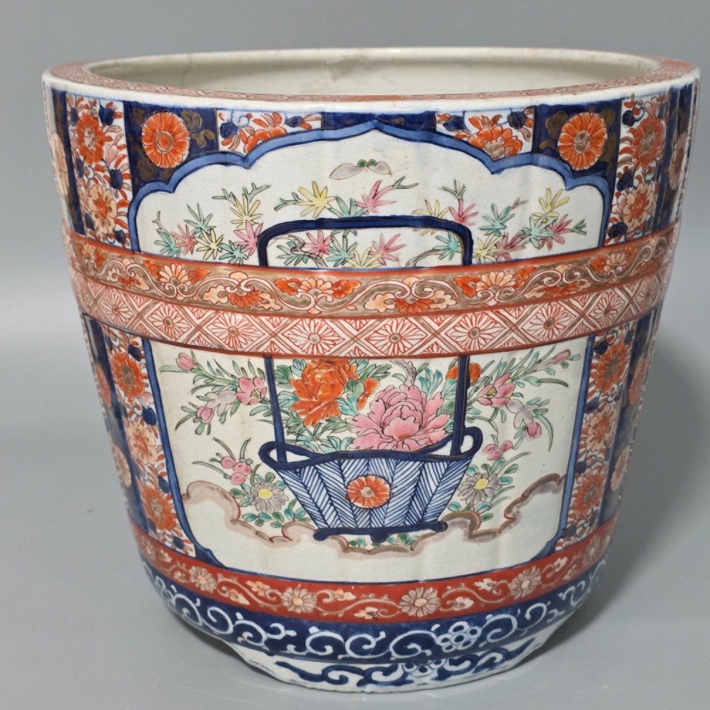 A late 19th-century Japanese Imari porcelain planter decorated with cobalt blue and iron-red floral basket panels, resting on a carved dark wood stand. View VIII