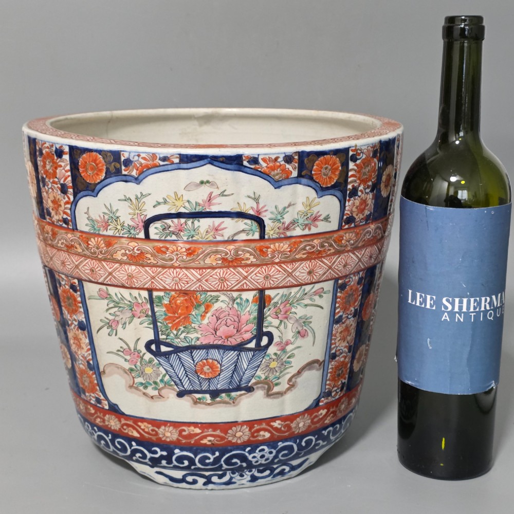 A late 19th-century Japanese Imari porcelain planter decorated with cobalt blue and iron-red floral basket panels, resting on a carved dark wood stand. View IX