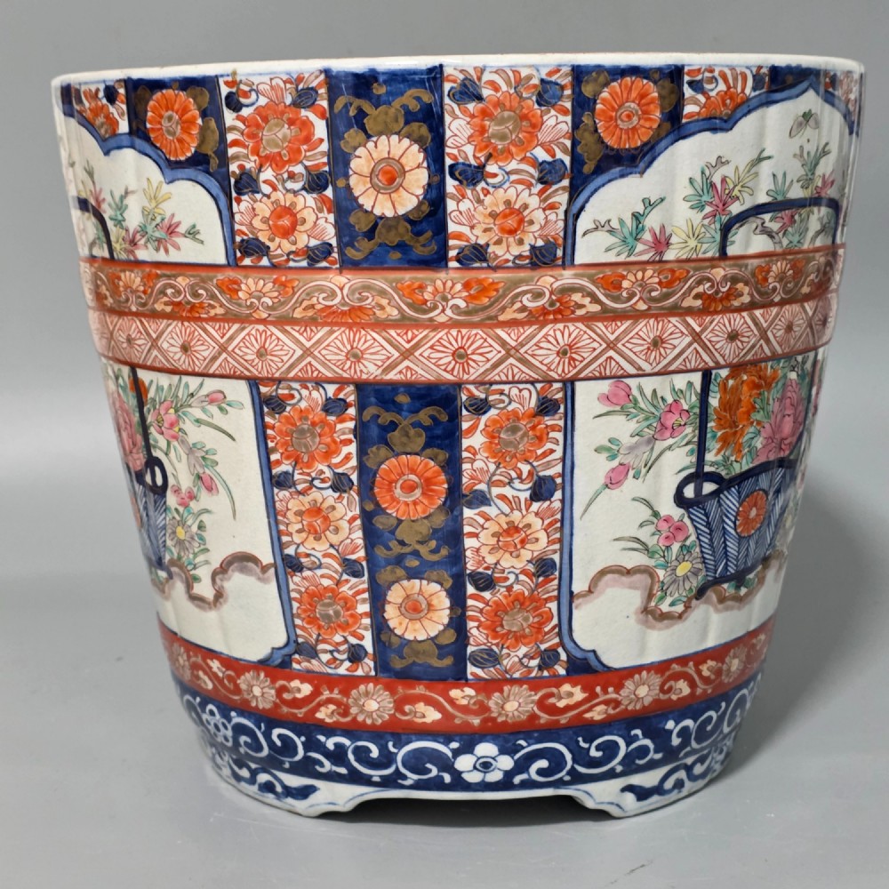 A late 19th-century Japanese Imari porcelain planter decorated with cobalt blue and iron-red floral basket panels, resting on a carved dark wood stand. View X