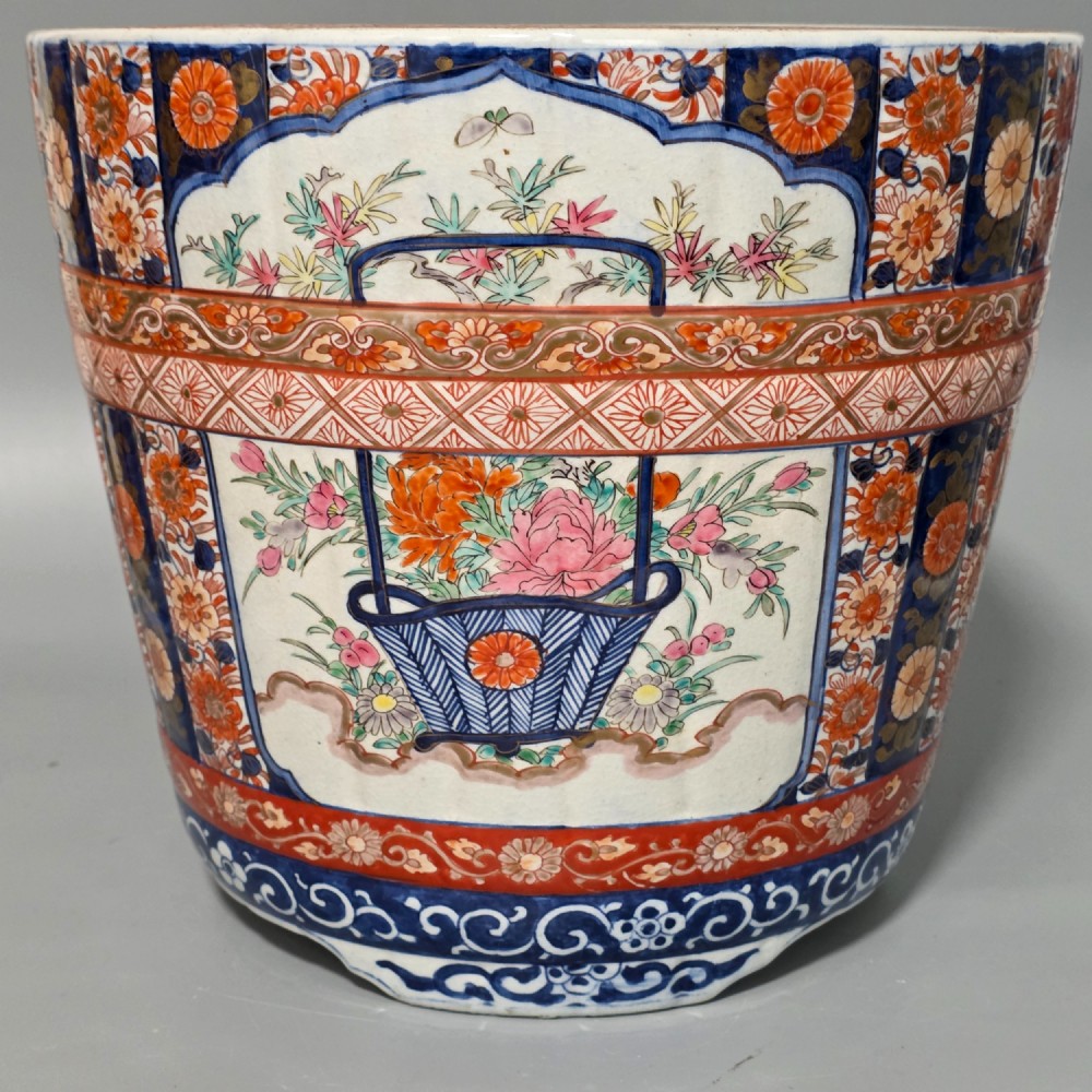 A late 19th-century Japanese Imari porcelain planter decorated with cobalt blue and iron-red floral basket panels, resting on a carved dark wood stand. View XI