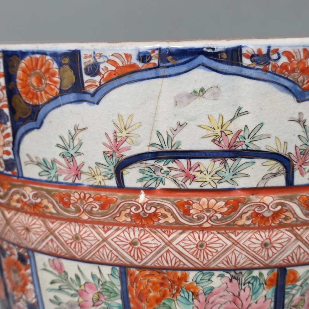 A late 19th-century Japanese Imari porcelain planter decorated with cobalt blue and iron-red floral basket panels, resting on a carved dark wood stand. View XIV