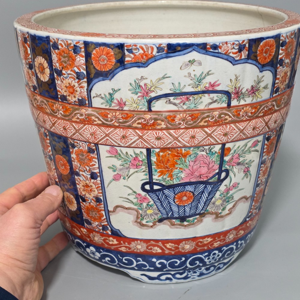 A late 19th-century Japanese Imari porcelain planter decorated with cobalt blue and iron-red floral basket panels, resting on a carved dark wood stand. View XV