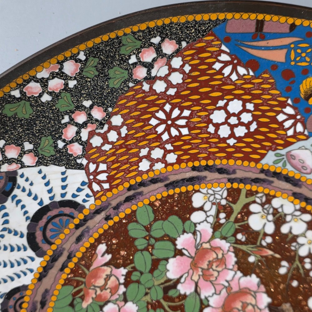 A circular Japanese cloisonne charger featuring a central medallion with birds and peonies on a brown aventurine background surrounded by patterned brocade sections. View V