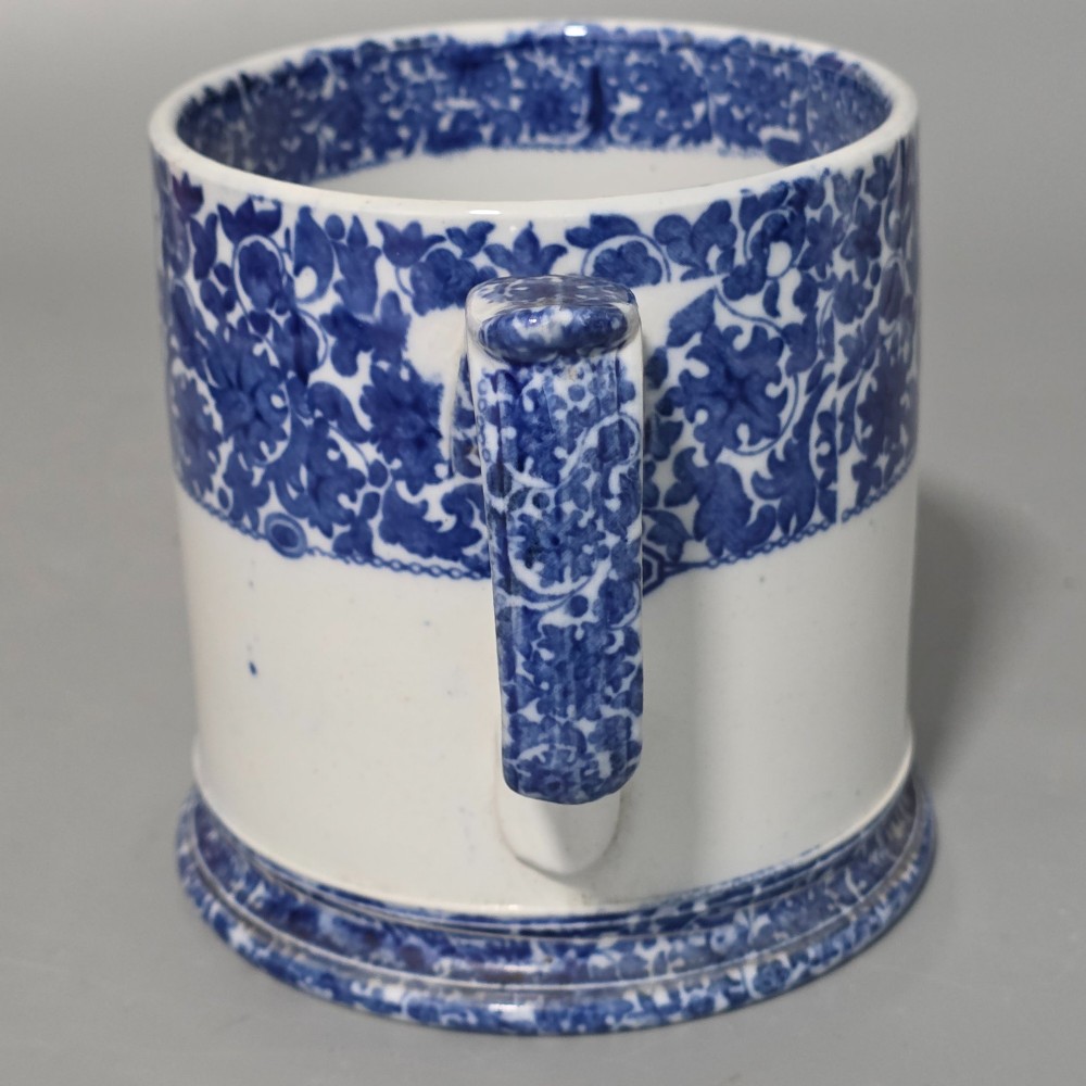 A cylindrical blue and white transferware ceramic tankard featuring a floral upper border and a coat of arms crest with the text No 11. View II