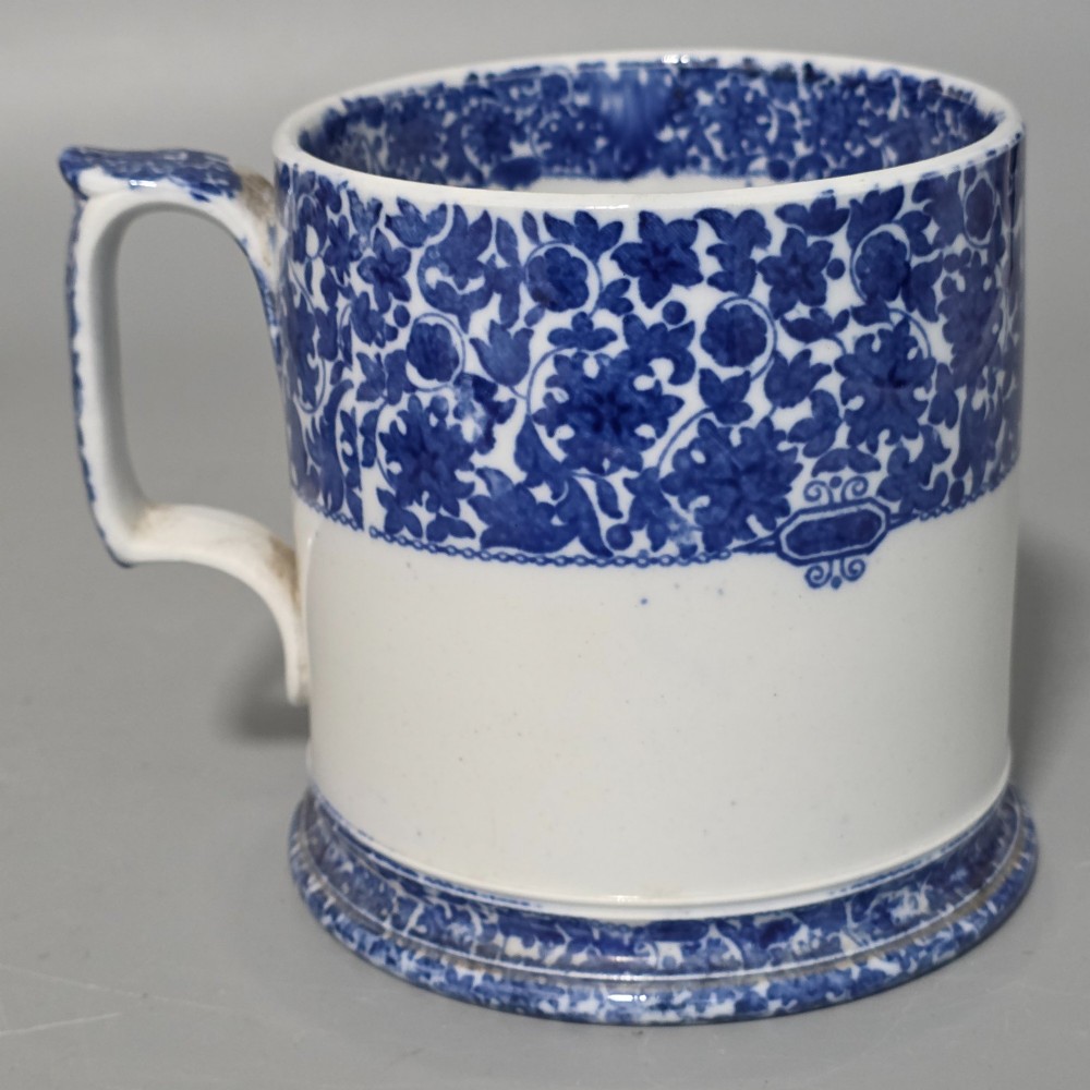 A cylindrical blue and white transferware ceramic tankard featuring a floral upper border and a coat of arms crest with the text No 11. View IX