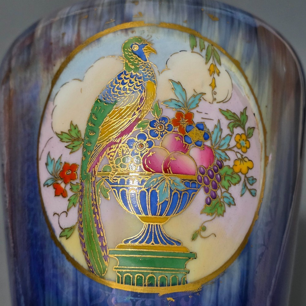 A tapered ceramic vase featuring a streaked iridescent blue lustre glaze and a central circular reserve illustrating a hand-enamelled parrot perched beside a fruit bowl. View II