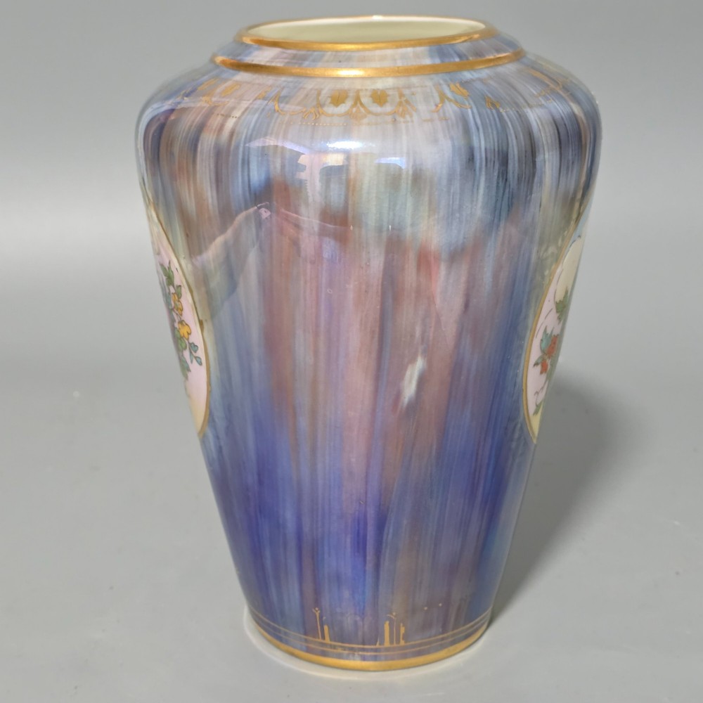 A tapered ceramic vase featuring a streaked iridescent blue lustre glaze and a central circular reserve illustrating a hand-enamelled parrot perched beside a fruit bowl. View III