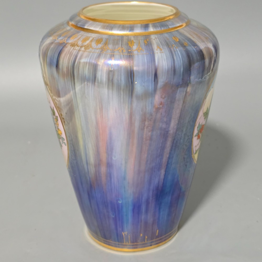 A tapered ceramic vase featuring a streaked iridescent blue lustre glaze and a central circular reserve illustrating a hand-enamelled parrot perched beside a fruit bowl. View VII