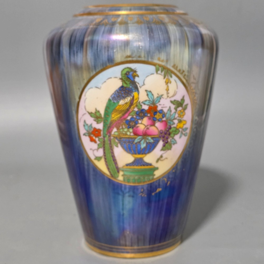 A tapered ceramic vase featuring a streaked iridescent blue lustre glaze and a central circular reserve illustrating a hand-enamelled parrot perched beside a fruit bowl. View VIII