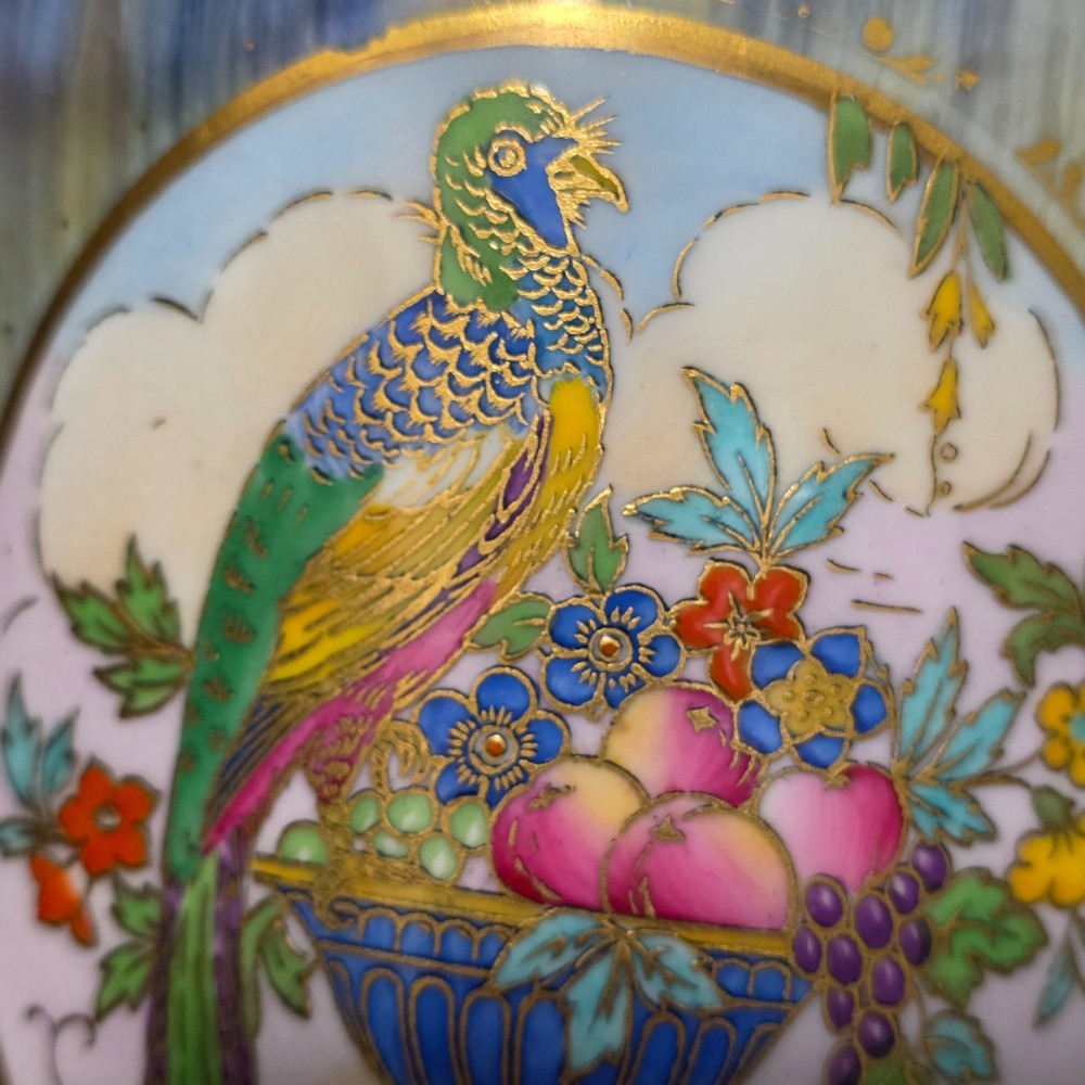 A tapered ceramic vase featuring a streaked iridescent blue lustre glaze and a central circular reserve illustrating a hand-enamelled parrot perched beside a fruit bowl. View XII
