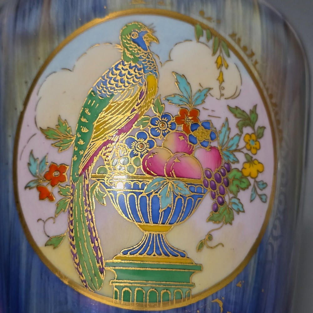 A tapered ceramic vase featuring a streaked iridescent blue lustre glaze and a central circular reserve illustrating a hand-enamelled parrot perched beside a fruit bowl. View XIII