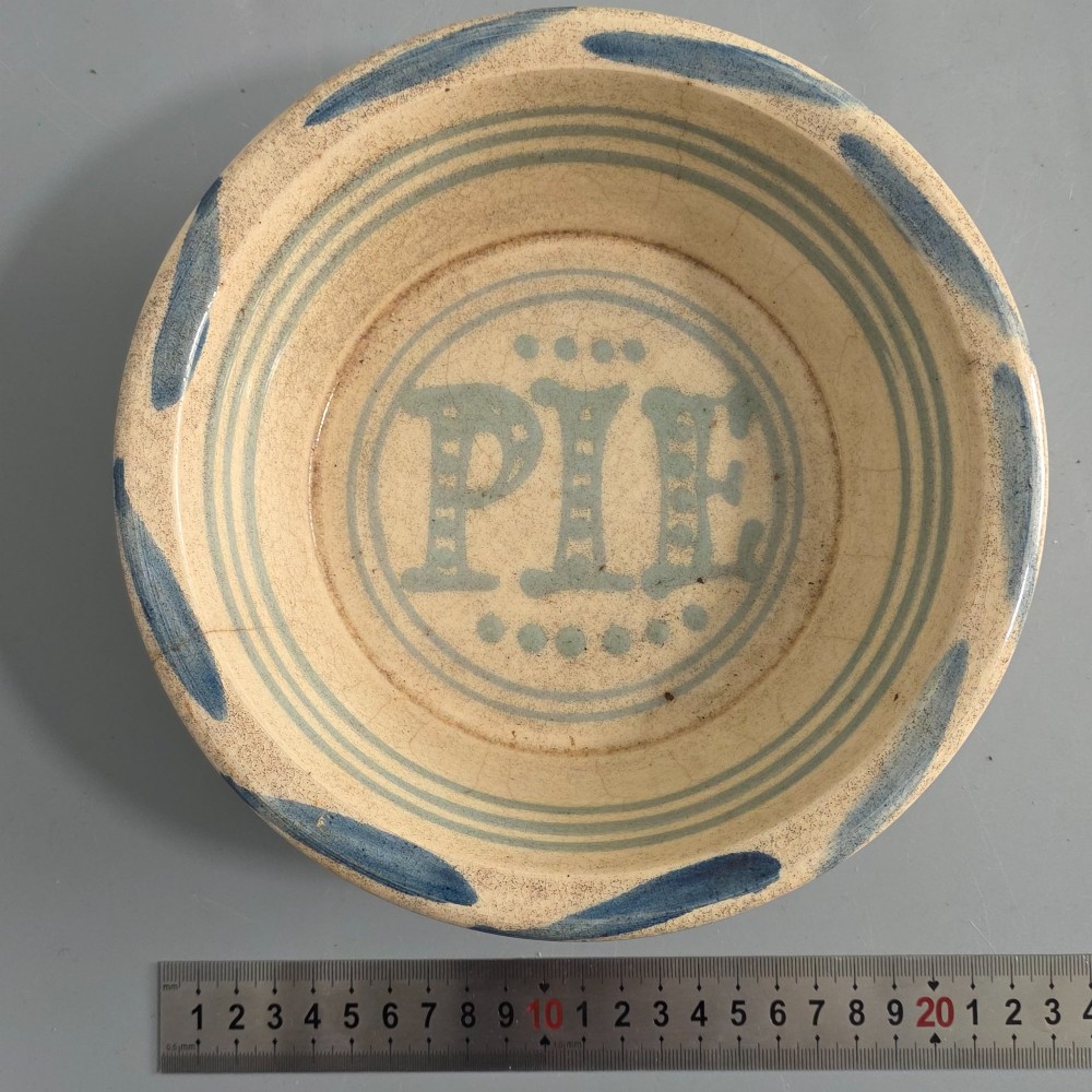 A circular nineteenth-century cream earthenware pie dish featuring the word PIE in blue lettering at the centre and blue decorative rim slashes. View II