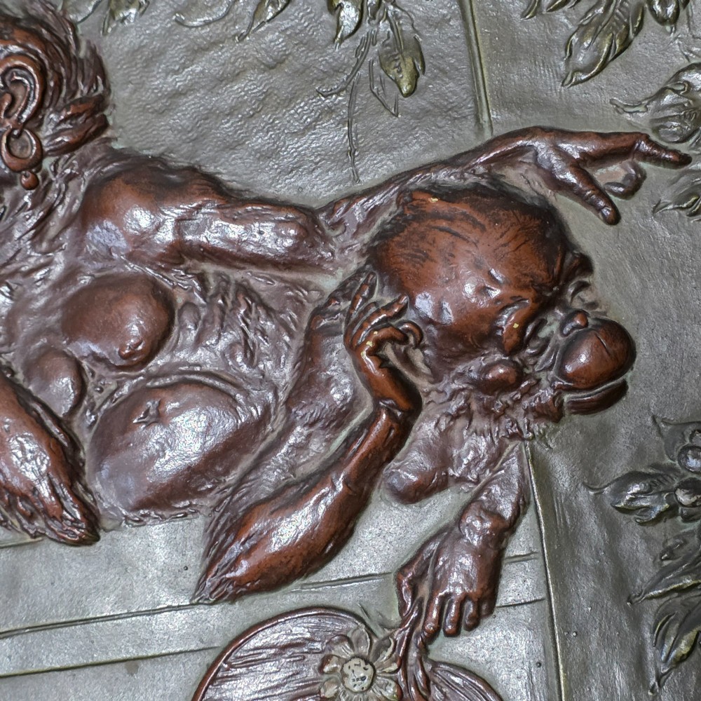 An oval dark brown Austrian terracotta relief plaque depicting a satirical scene of an anthropomorphic monkey family framed by relief floral motifs. View VI