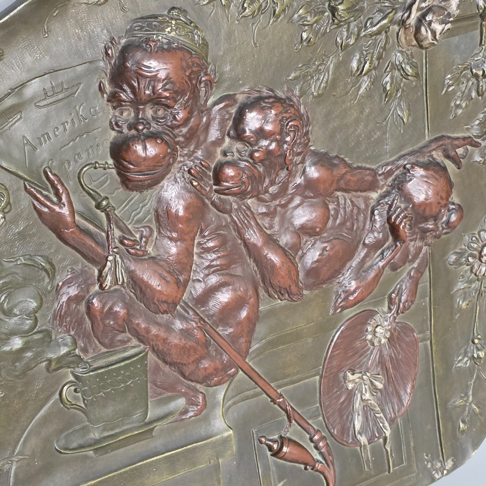 An oval dark brown Austrian terracotta relief plaque depicting a satirical scene of an anthropomorphic monkey family framed by relief floral motifs. View IX
