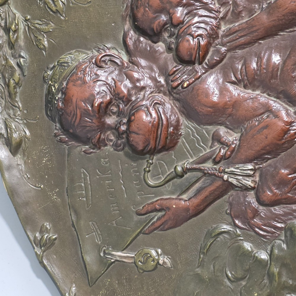 An oval dark brown Austrian terracotta relief plaque depicting a satirical scene of an anthropomorphic monkey family framed by relief floral motifs. View XII