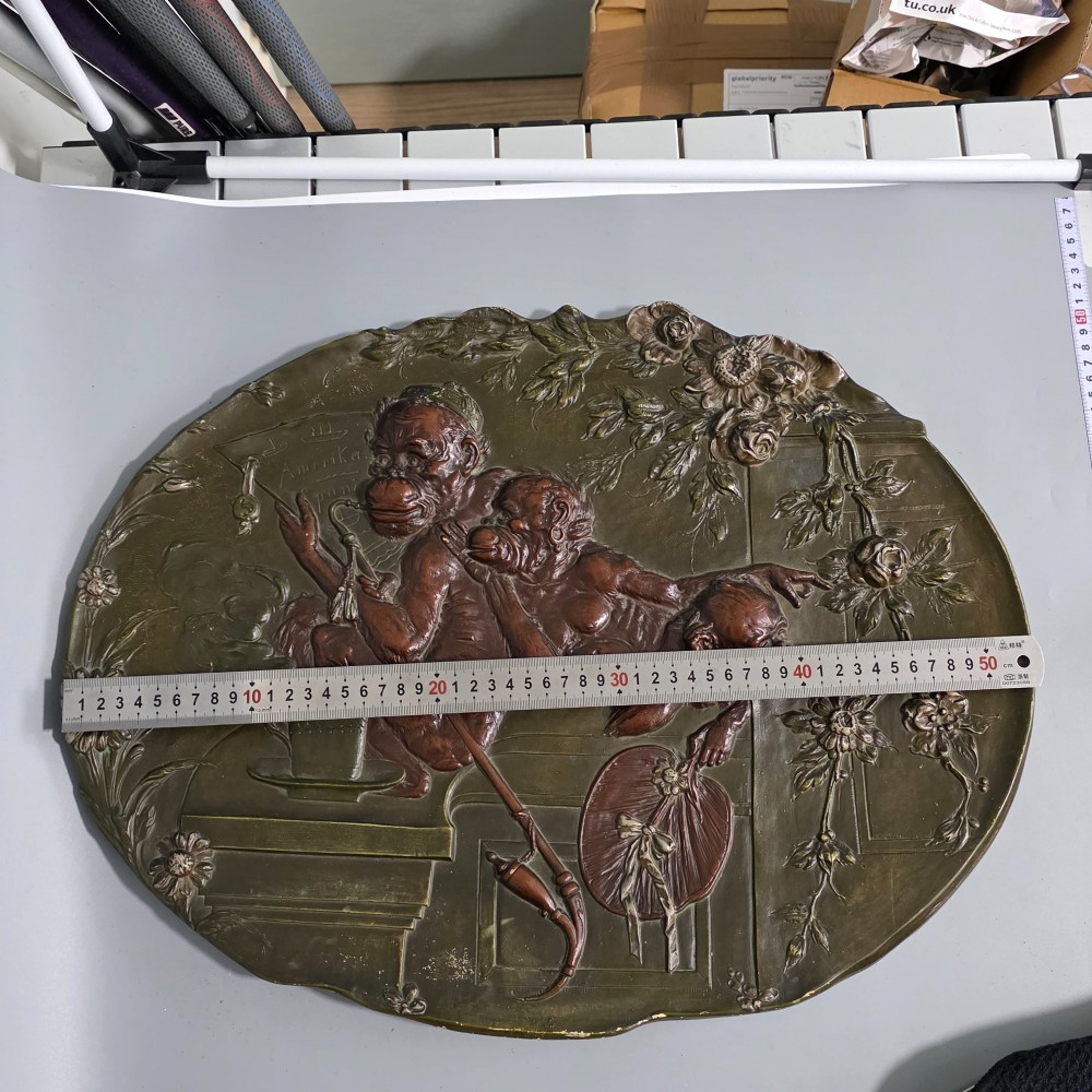 An oval dark brown Austrian terracotta relief plaque depicting a satirical scene of an anthropomorphic monkey family framed by relief floral motifs. View II