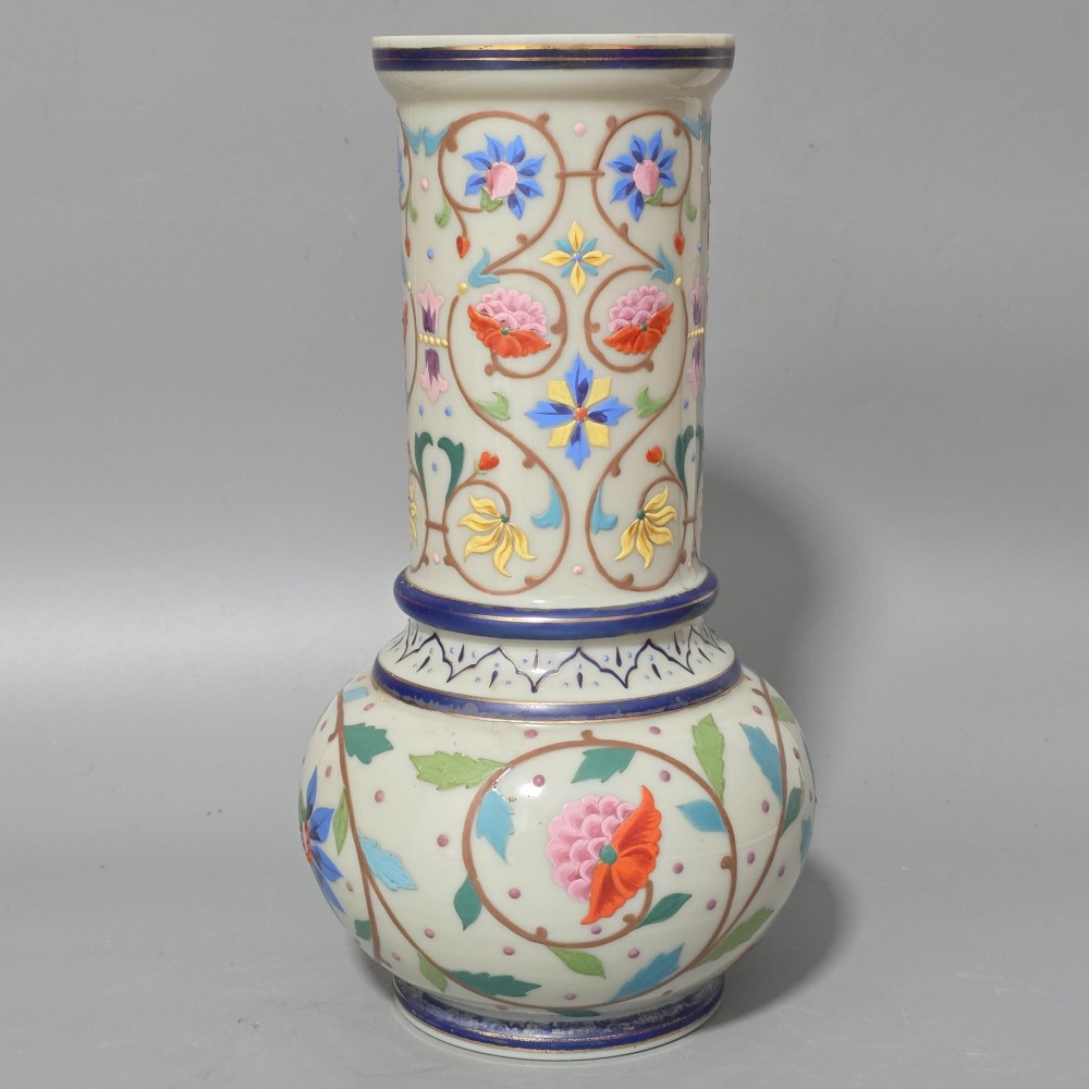 An antique cream opaque glass vase featuring hand-painted floral arabesque enamel patterns in bright colours with gilded accents and cobalt blue bands.