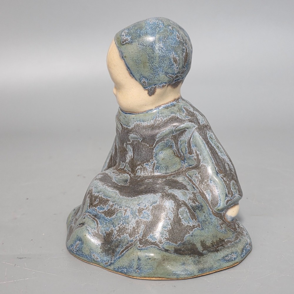 A glazed stoneware figurine depicting a seated child wearing a bonnet, rendered with a mottled blue and grey glaze and a smooth cream face. View VI