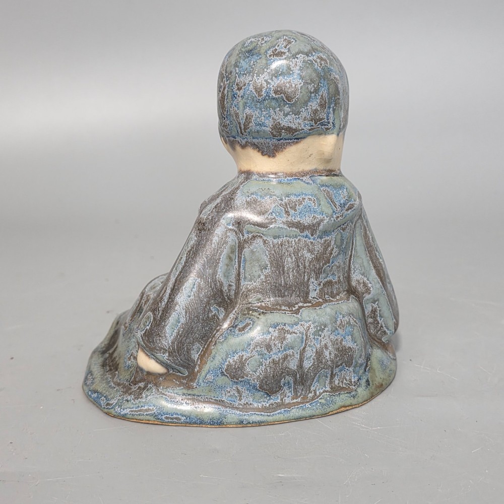 A glazed stoneware figurine depicting a seated child wearing a bonnet, rendered with a mottled blue and grey glaze and a smooth cream face. View VIII