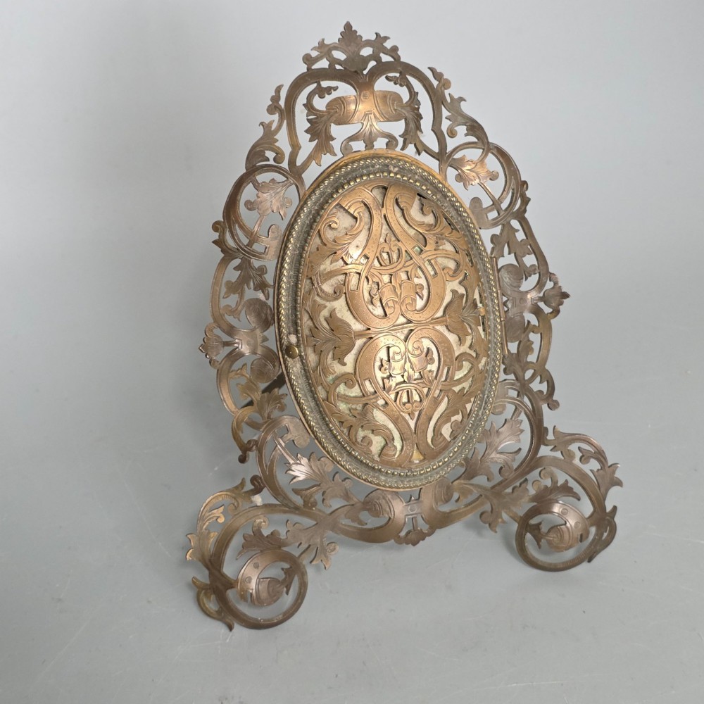 An ornate late Victorian easel photo frame crafted from pierced brass scrollwork with a central hinged oval door.