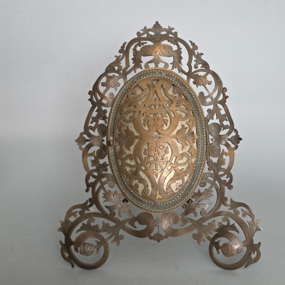An ornate late Victorian easel photo frame crafted from pierced brass scrollwork with a central hinged oval door. View II