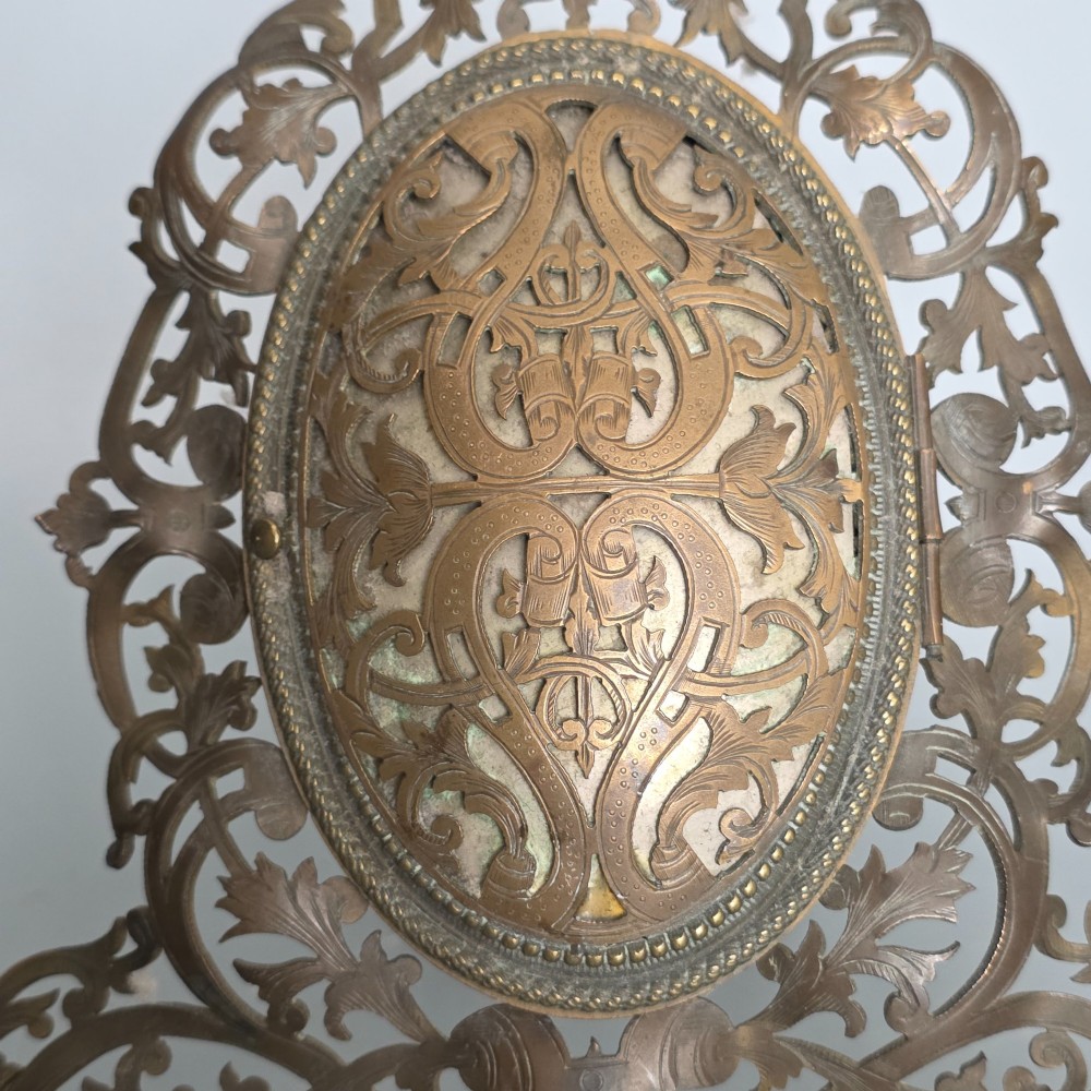 An ornate late Victorian easel photo frame crafted from pierced brass scrollwork with a central hinged oval door. View III