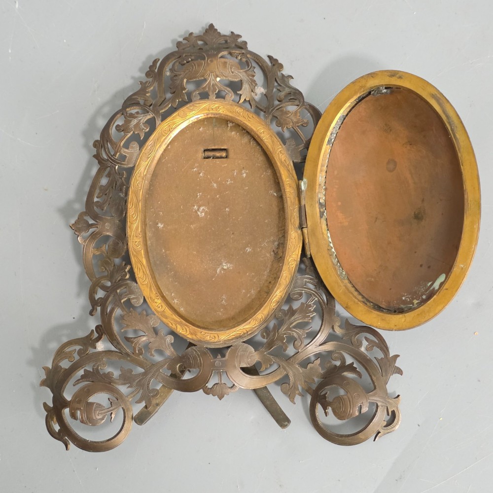 An ornate late Victorian easel photo frame crafted from pierced brass scrollwork with a central hinged oval door. View IV