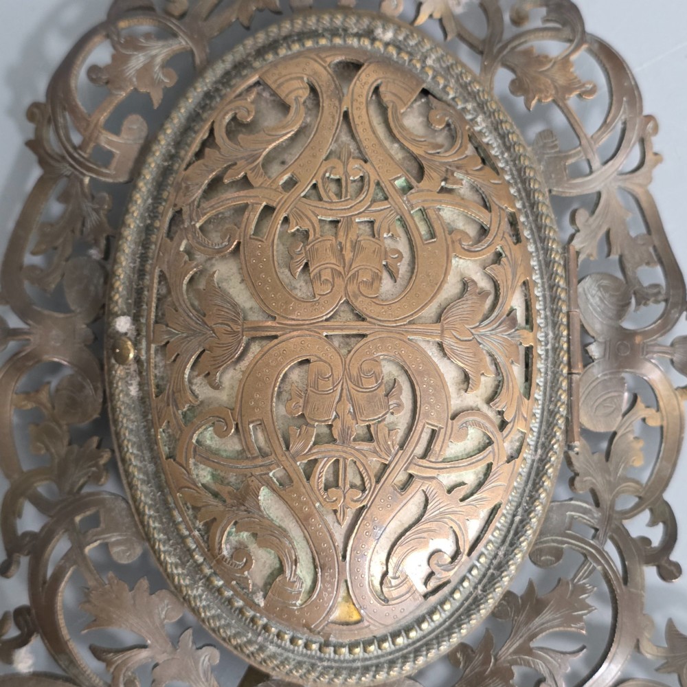 An ornate late Victorian easel photo frame crafted from pierced brass scrollwork with a central hinged oval door. View V