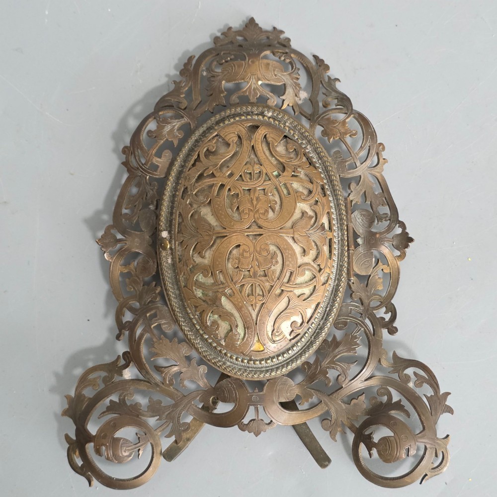 An ornate late Victorian easel photo frame crafted from pierced brass scrollwork with a central hinged oval door. View VI