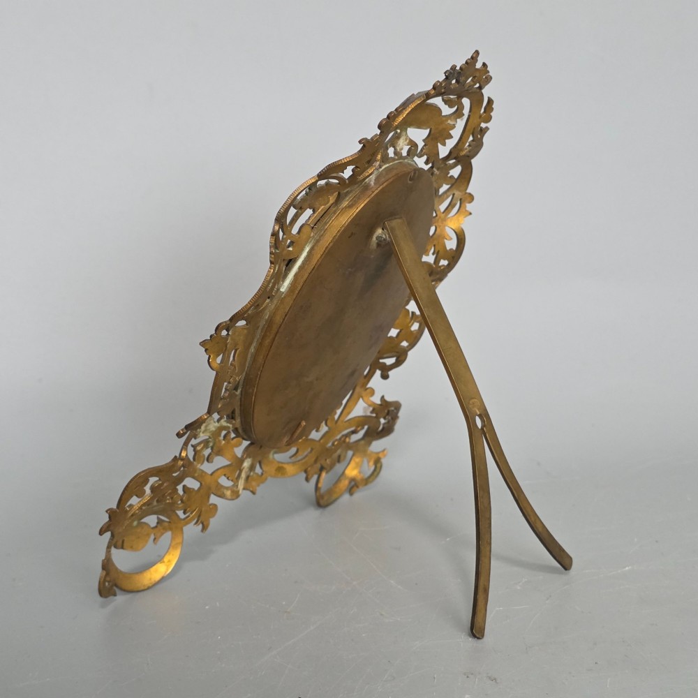 An ornate late Victorian easel photo frame crafted from pierced brass scrollwork with a central hinged oval door. View VIII