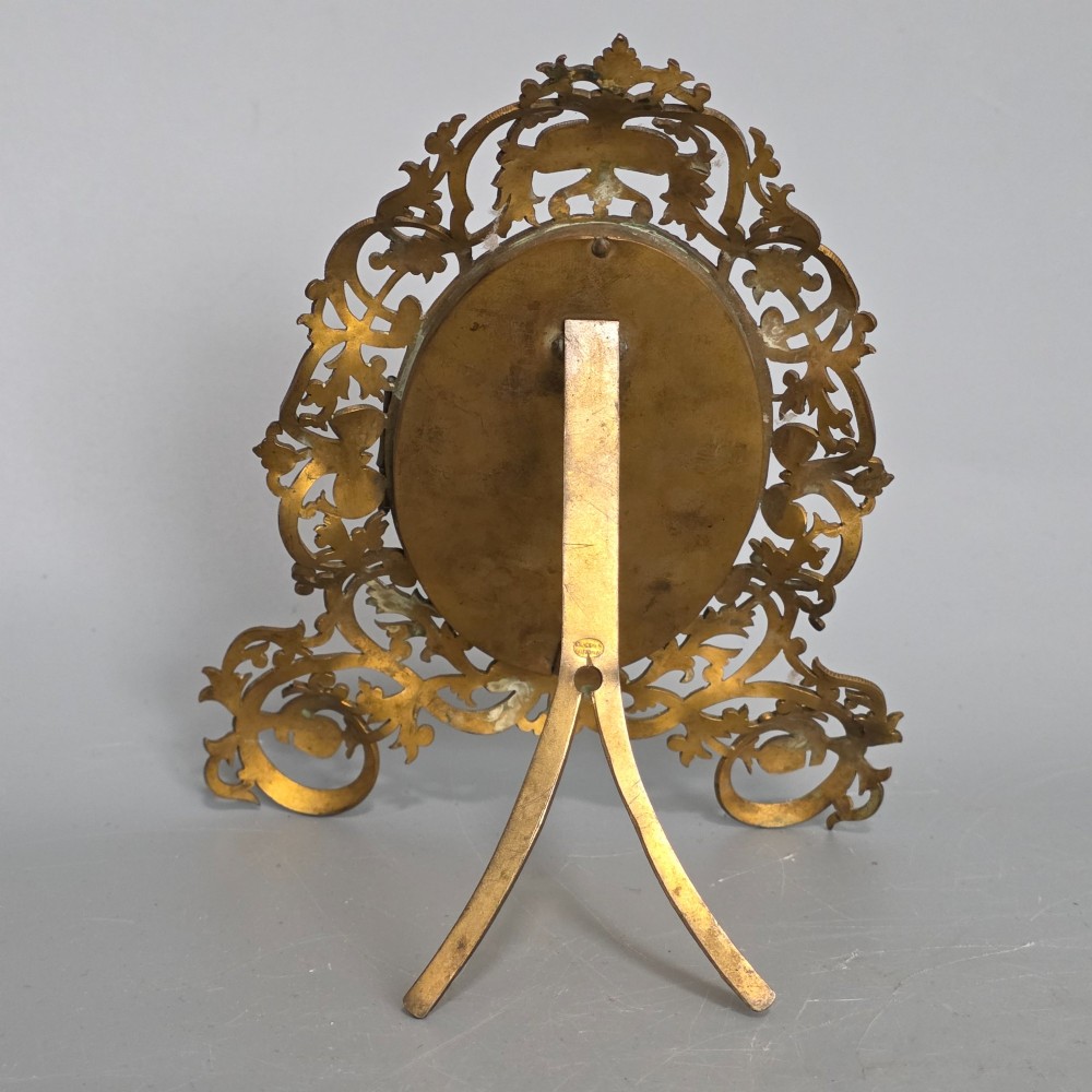 An ornate late Victorian easel photo frame crafted from pierced brass scrollwork with a central hinged oval door. View IX