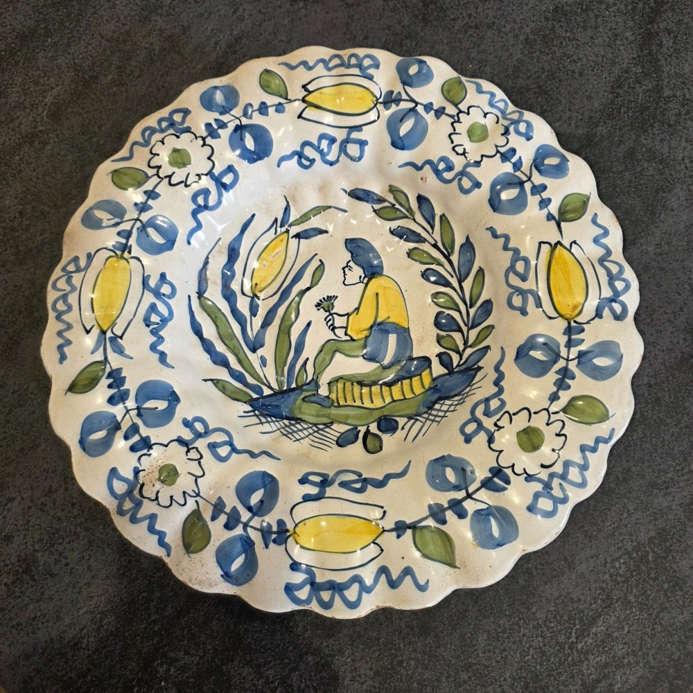 A 17th-century Dutch Delftware lobed ceramic dish hand-painted with a blue, yellow, and green floral border and a central figure.