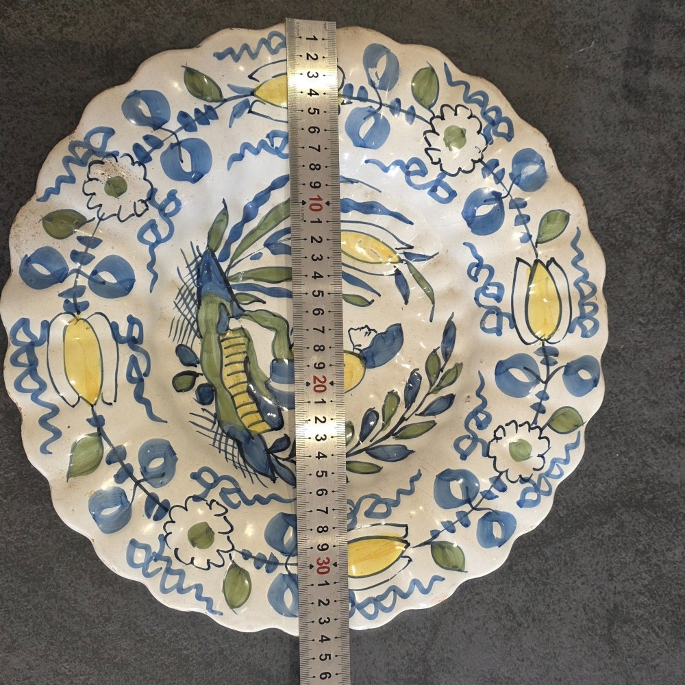 A 17th-century Dutch Delftware lobed ceramic dish hand-painted with a blue, yellow, and green floral border and a central figure. View II