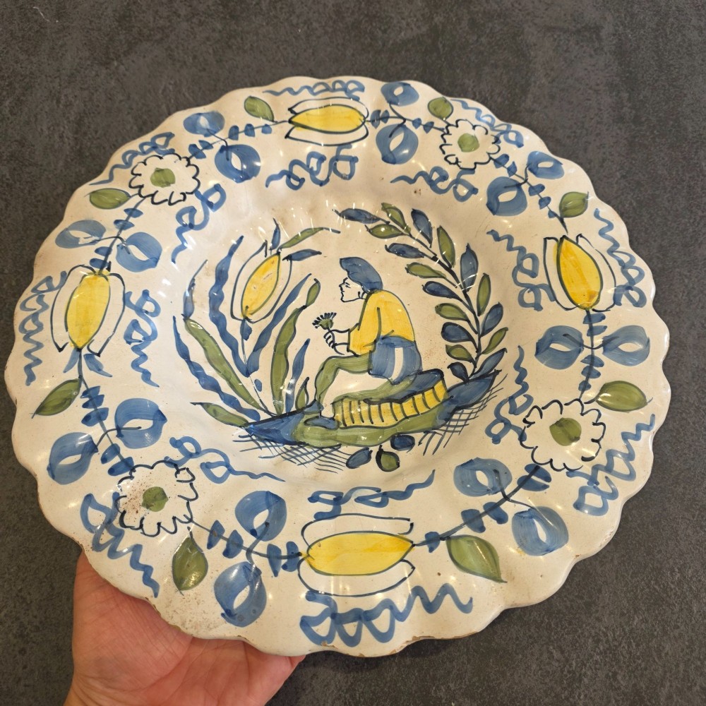 A 17th-century Dutch Delftware lobed ceramic dish hand-painted with a blue, yellow, and green floral border and a central figure. View III