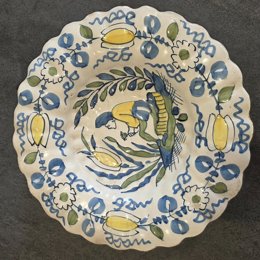 A 17th-century Dutch Delftware lobed ceramic dish hand-painted with a blue, yellow, and green floral border and a central figure. View IV