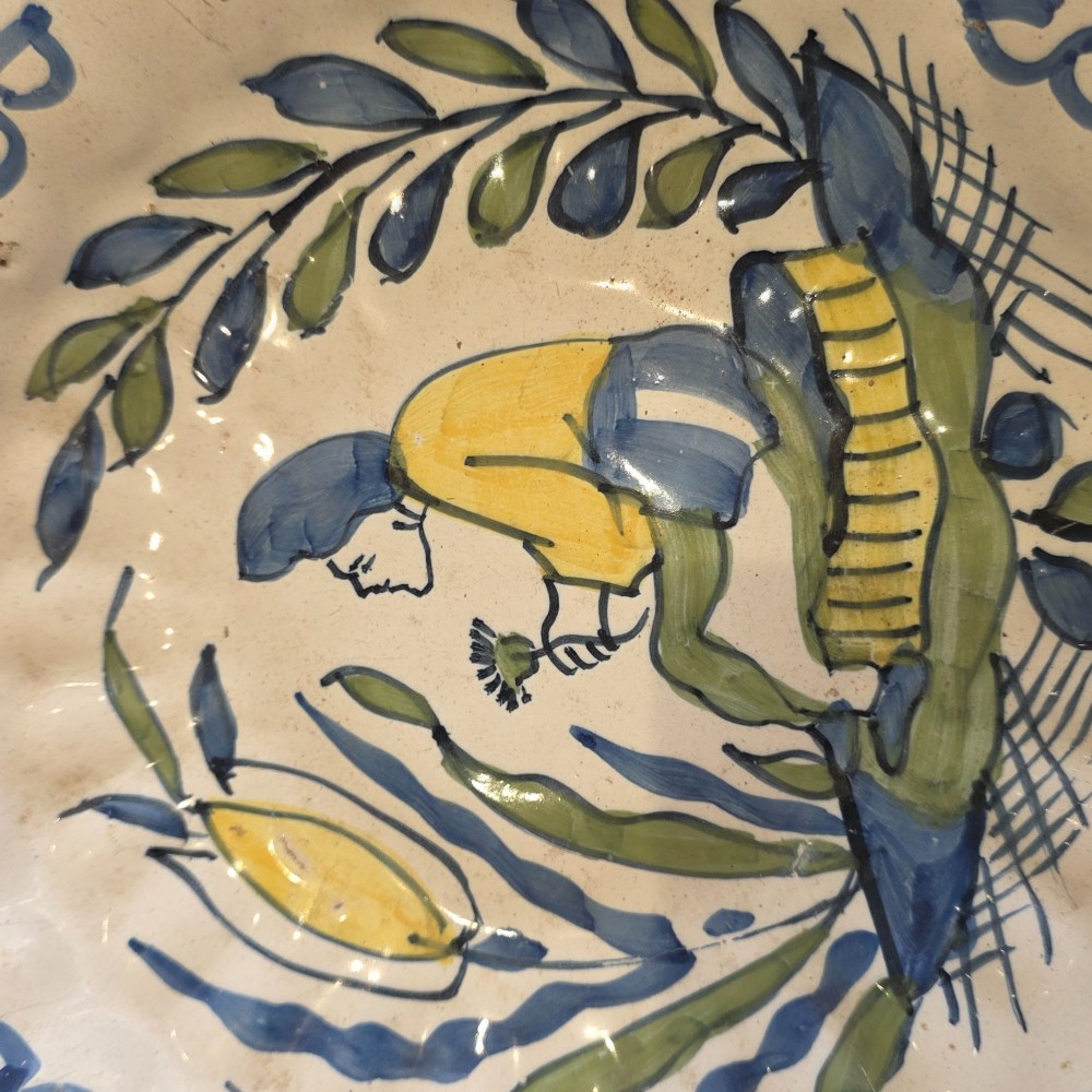 A 17th-century Dutch Delftware lobed ceramic dish hand-painted with a blue, yellow, and green floral border and a central figure. View V