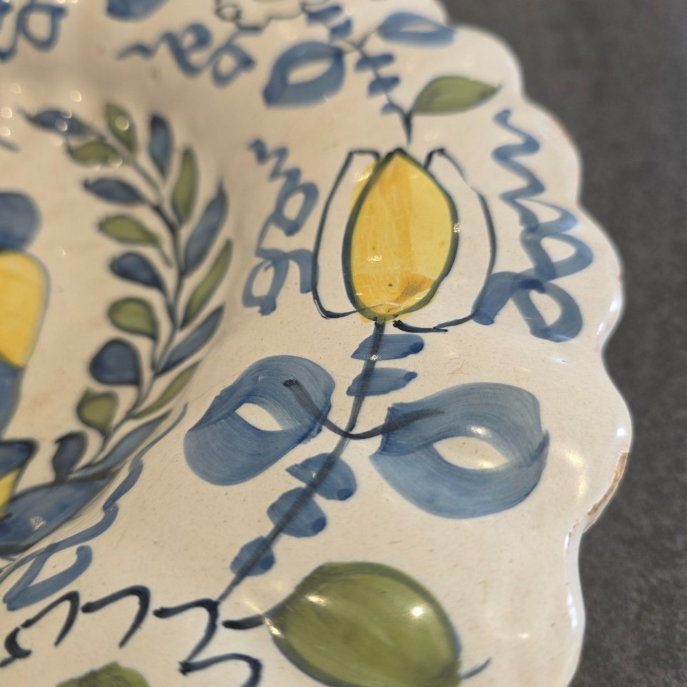 A 17th-century Dutch Delftware lobed ceramic dish hand-painted with a blue, yellow, and green floral border and a central figure. View VI