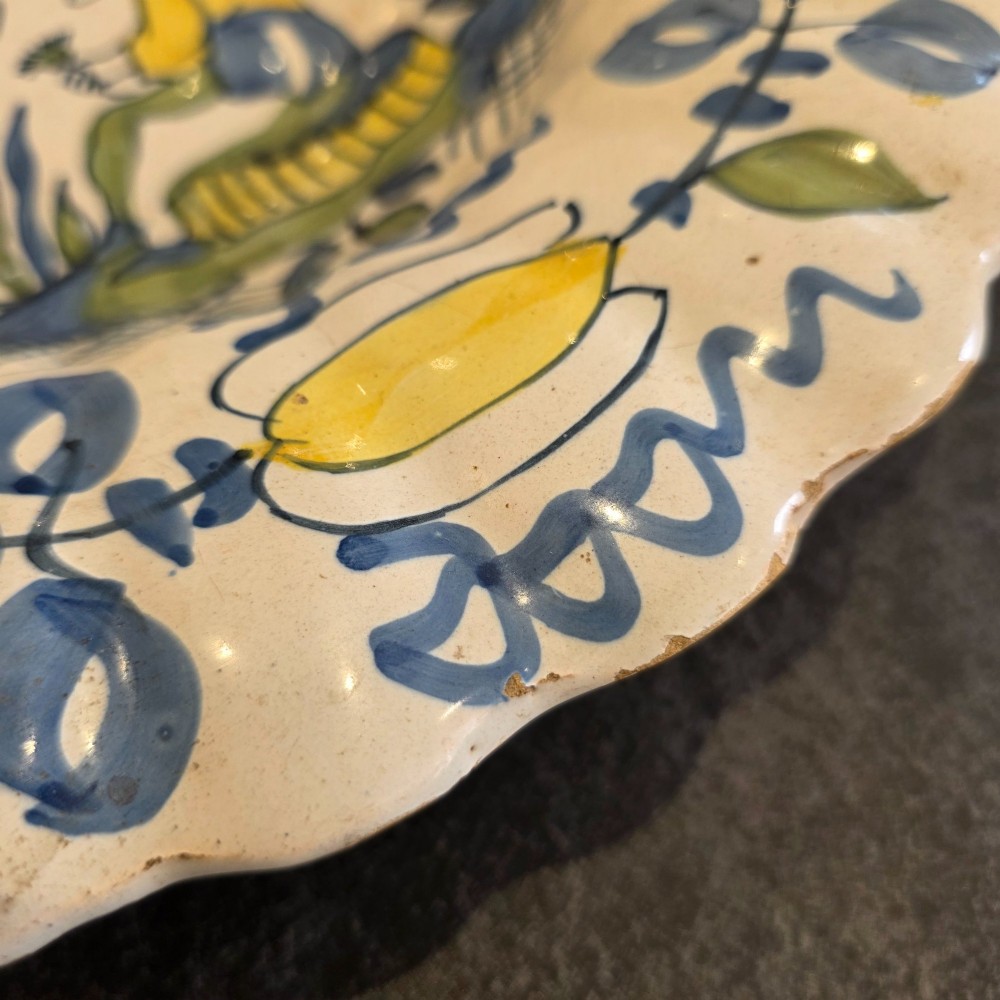 A 17th-century Dutch Delftware lobed ceramic dish hand-painted with a blue, yellow, and green floral border and a central figure. View VII