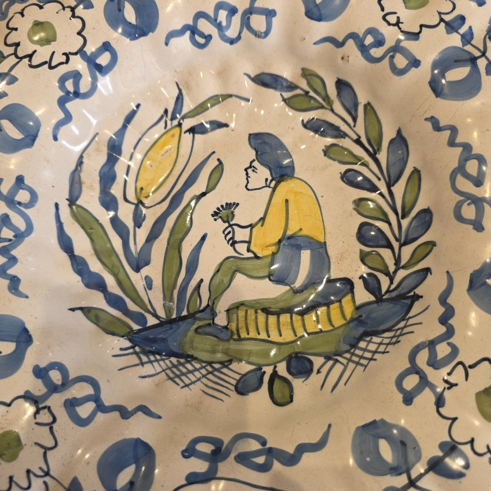 A 17th-century Dutch Delftware lobed ceramic dish hand-painted with a blue, yellow, and green floral border and a central figure. View VIII