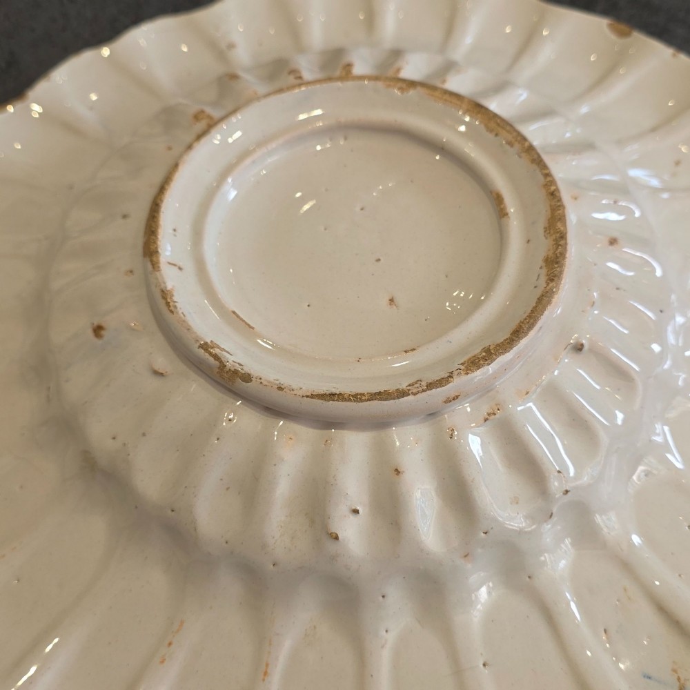 A 17th-century Dutch Delftware lobed ceramic dish hand-painted with a blue, yellow, and green floral border and a central figure. View X