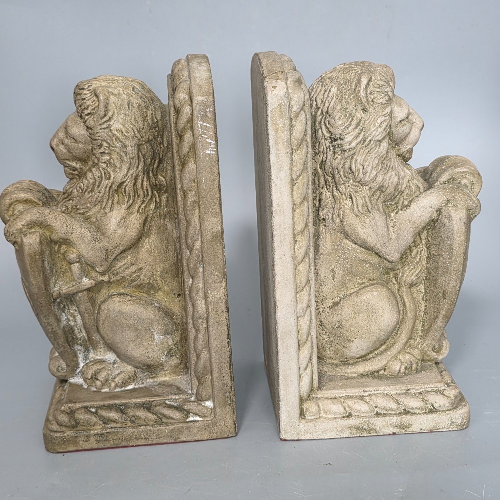 A pair of grey cast stone bookends sculpted as seated lions holding shields featuring a fleur-de-lis motif. View II
