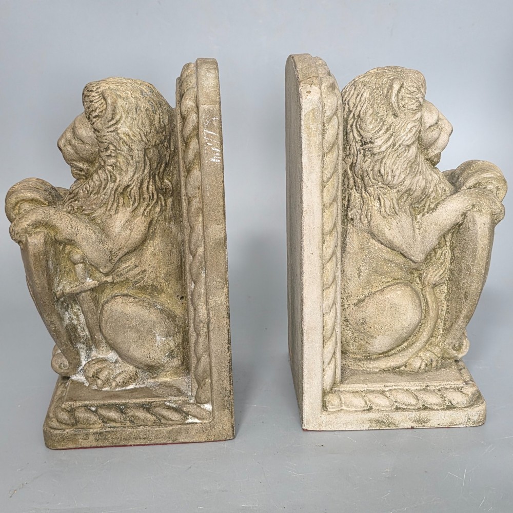 A pair of grey cast stone bookends sculpted as seated lions holding shields featuring a fleur-de-lis motif. View IV