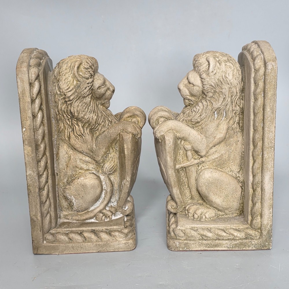 A pair of grey cast stone bookends sculpted as seated lions holding shields featuring a fleur-de-lis motif. View V