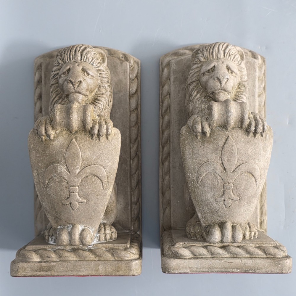A pair of grey cast stone bookends sculpted as seated lions holding shields featuring a fleur-de-lis motif. View VI