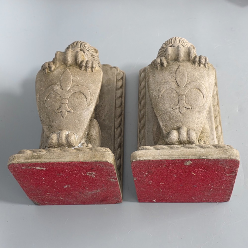 A pair of grey cast stone bookends sculpted as seated lions holding shields featuring a fleur-de-lis motif. View VII