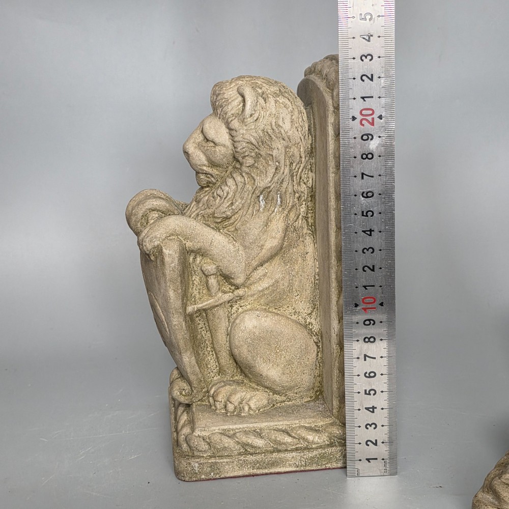 A pair of grey cast stone bookends sculpted as seated lions holding shields featuring a fleur-de-lis motif. View IX