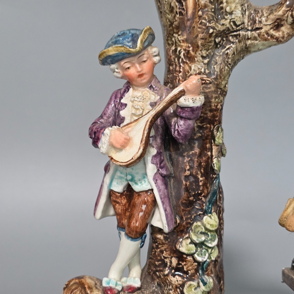 A Victorian majolica spill holder shaped as a hollow tree trunk with a figure of a man playing a lute next to a woman suspended on a swing. View II